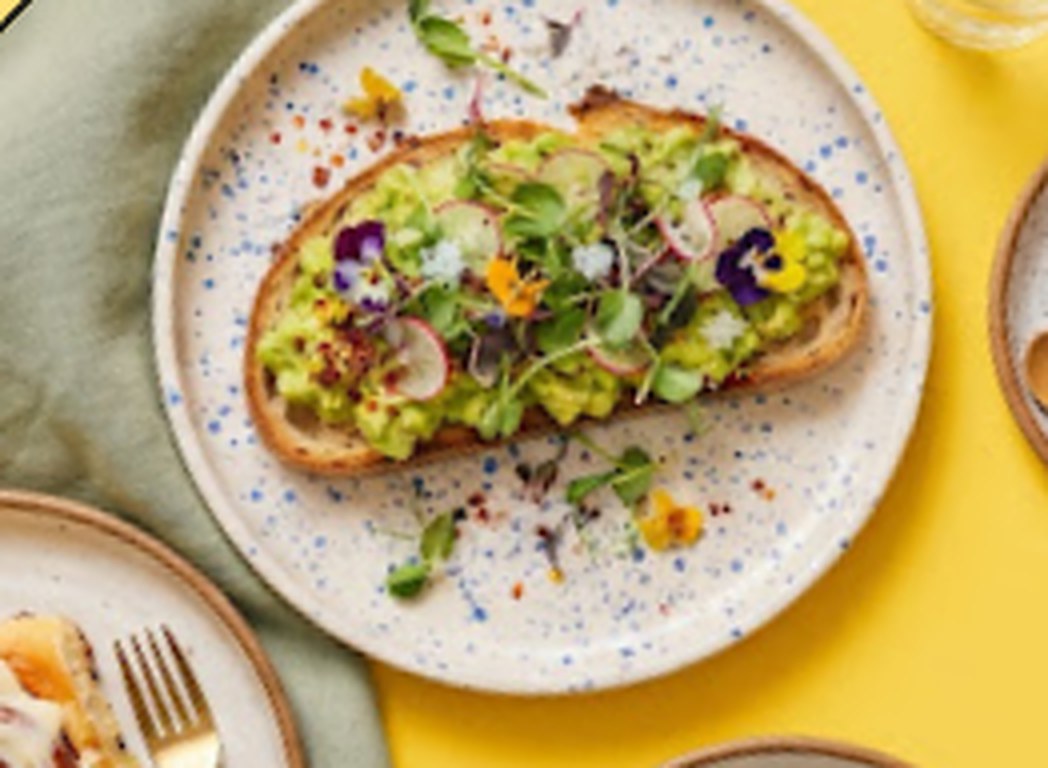 Tosta de aguacate con flores comestibles y café con leche vegetal sobre mesa amarilla